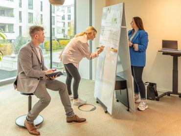Ein Mann und zwei Frauen arbeiten während Meeting an Whiteboard