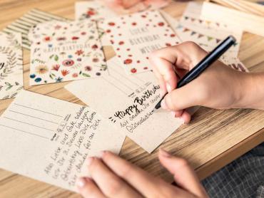 Frau schreibt mit der Hand eine Geburtstagskarte