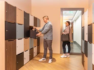 Ein Mann und eine Frau verstauen Desk Sharing Bag in Locker