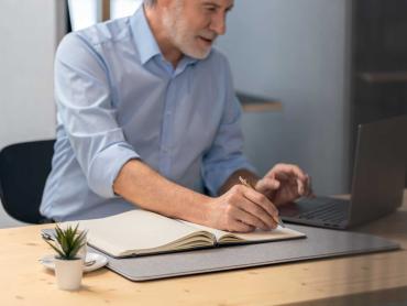 Mann arbeitet an Laptop und schreibt in Notizbuch