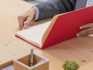 Ein Notizbuch in rot liegt halboffen auf dem Tisch