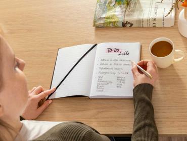 Frau schreibt To-Do-Liste in Notizbuch