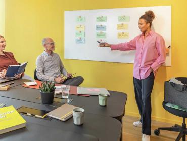 Frau analysiert gemeinsam mit zwei Kollegen Projektverlauf mit Hilfe von Glas-Whiteboard