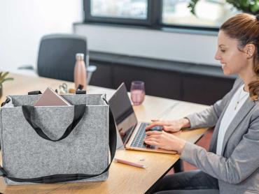 Frau sitzt lächelnd an Schreibtisch mit Desk Sharing Bag und tippt auf Laptop