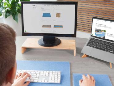 Mann sitzt an Schreibtisch mit Monitor auf Monitorständer und Laptop in Laptopständer