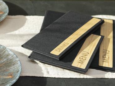 Drei Speisekartenmappen mit echtem Holz liegen auf dem gedeckten Tisch im Restaurant