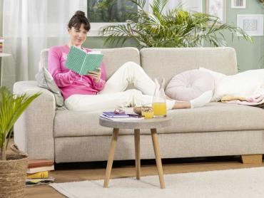 Frau in rosa Pulli sitzt Zuhause auf Sofa und schreibt in Jolie Notizbuch
