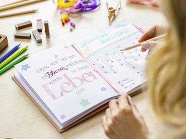 Frau schreibt mit Buntstiften schönen Spruch und Stimmungstracker in Jolie Notizbuch auf Schreibtisch