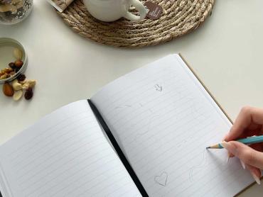 Hand zeichnet Doodles in Notizbuch, daneben stehen Nüsse