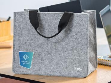 Hellgraue Desk Sharing Bag aus Filz mit blauem Logoaufdruck steht auf dem Schreibtisch