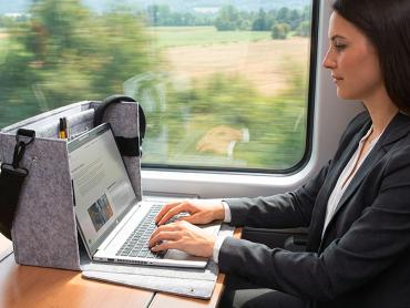 Eine Frau arbeitet im Zug am Tisch an ihrem Laptop. Der Laptop steht in der Workspace Desk Sharing Bag.