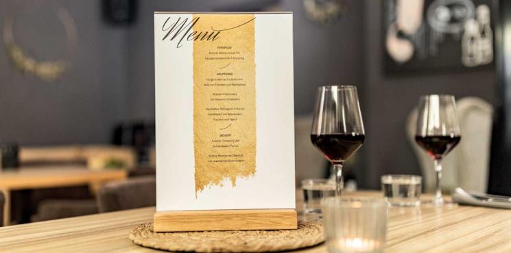 Infoaufsteller mit Menü auf Tisch und zwei Weingläser