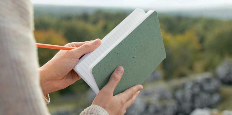 Frau hält Re-Up Notizbuch in der Natur in den Händen