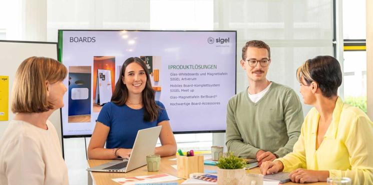 Kollegen stehen an Tisch vor Monitor und besprechen sich