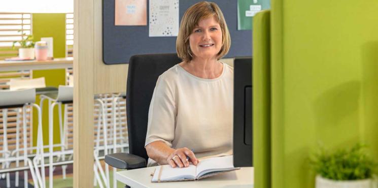 Frau arbeitet an Schreibtisch und blickt in Kamera