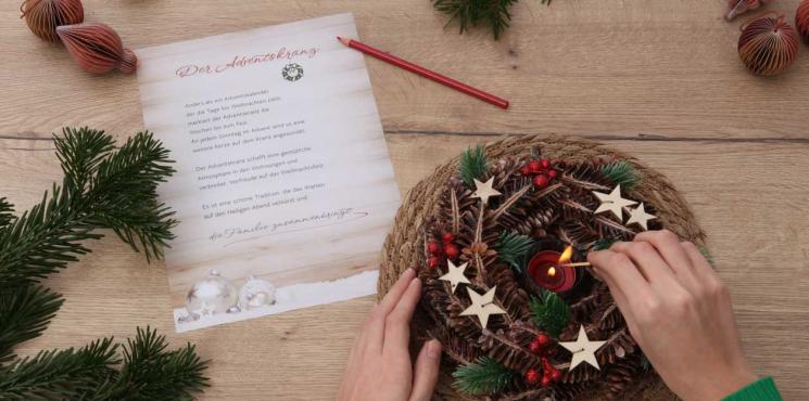 Händen zünden Kerze in Weihnachtskranz an