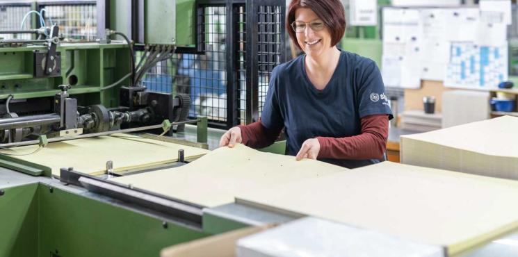 Frau arbeitet an Weiterverarbeitungsmaschine in Druckerei