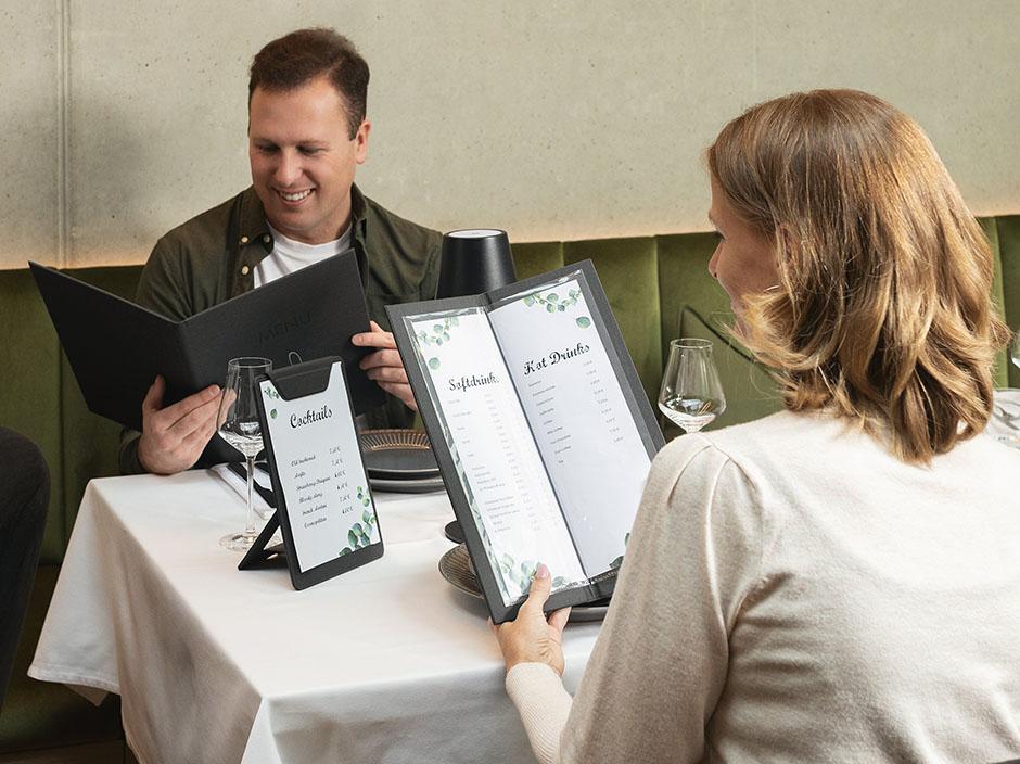 Mann und Frau sitzen im Restauran am Tisch und betrachten die Speisekarten