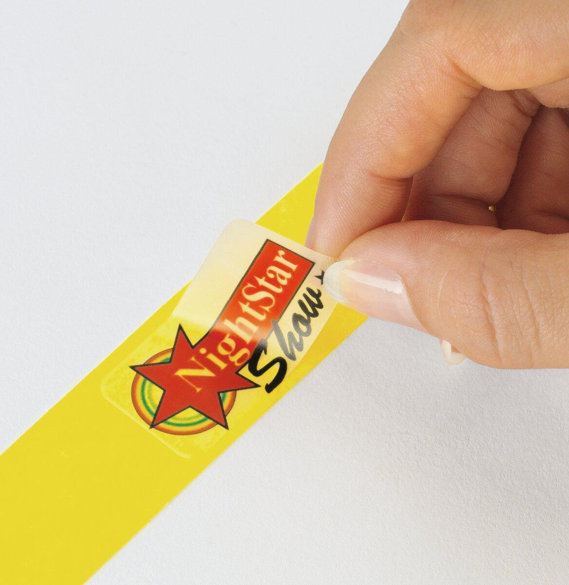 A hand peels off a see-through label with NightStar Show from a yellow background