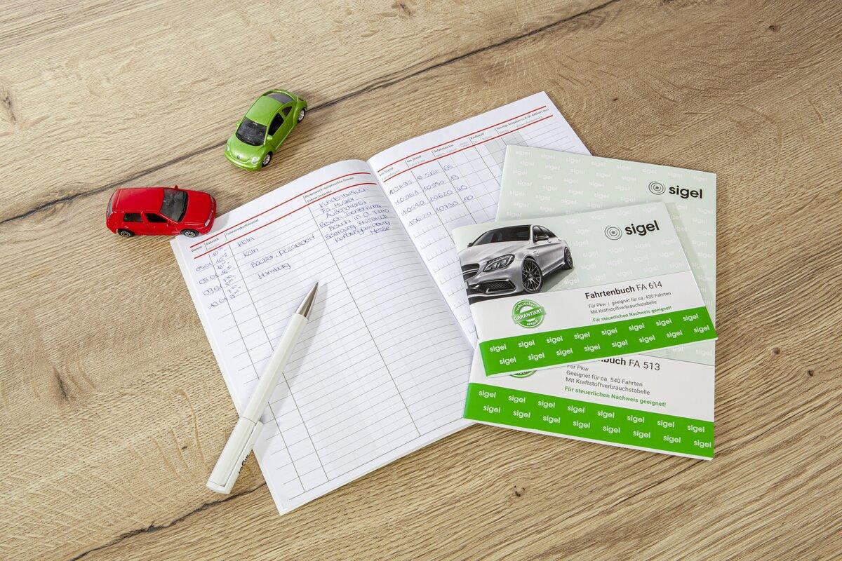 Heft mit schriftlichen Notizen, daneben zwei Spielzeugautos und ein Kugelschreiber auf Holztisch