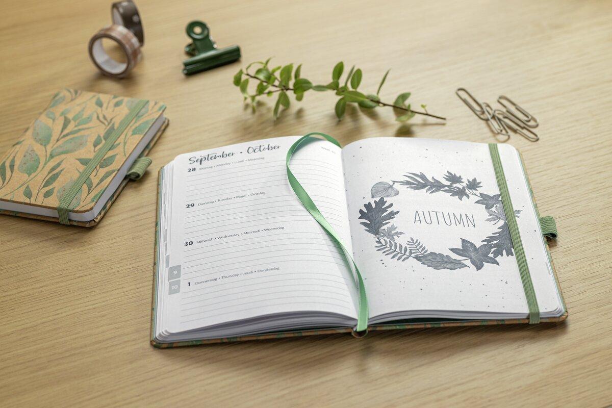 Notizbuch mit herbstlichem Motiv, Zweig und Büroklammern auf Tisch