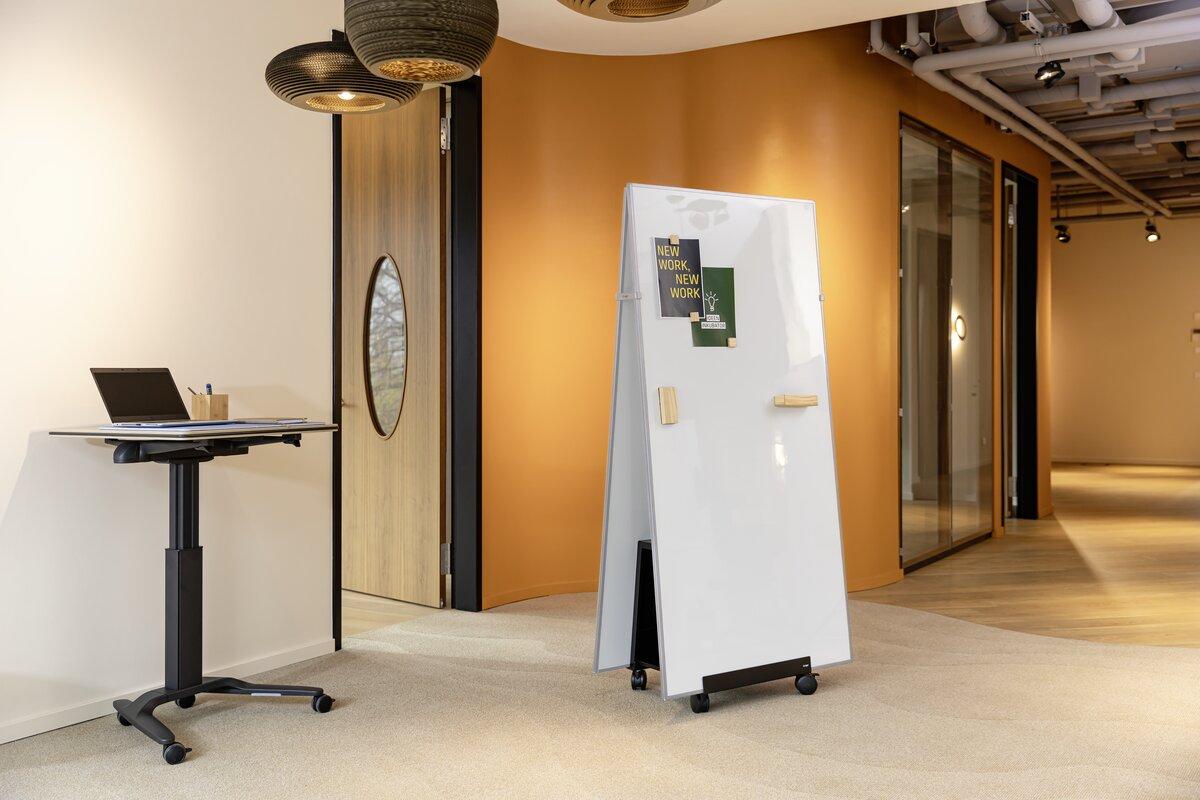 Laptop on high table, next to double-sided board with magnets in office environment