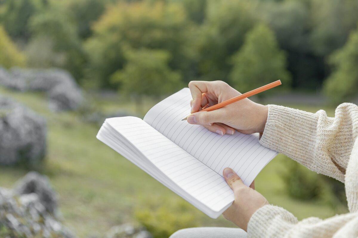 Hand schreibt mit Stift in Notizbuch, Hintergrund Natur
