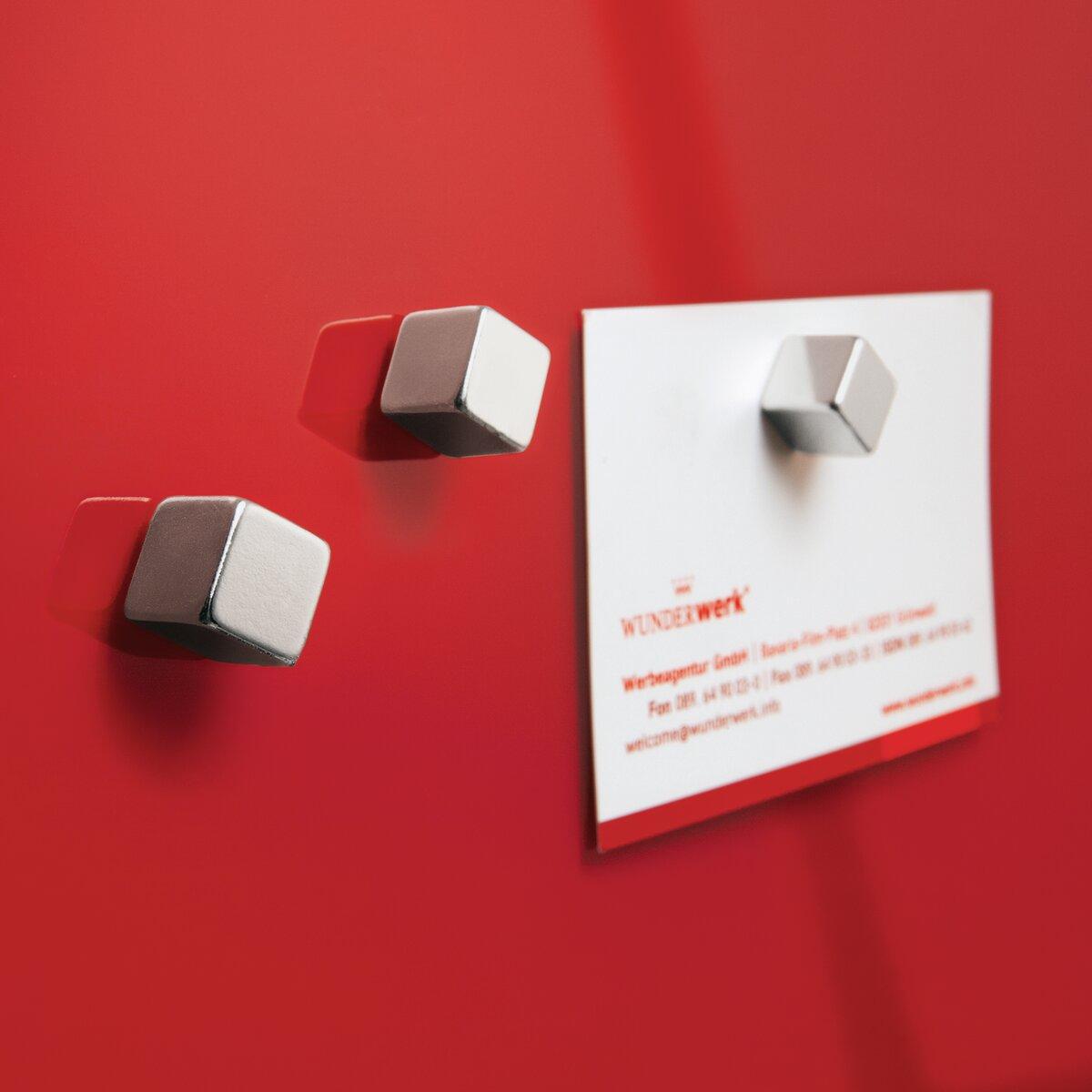 Silberne Magnete auf rotem Hintergrund, ein Magnet hält ein weißes Papier