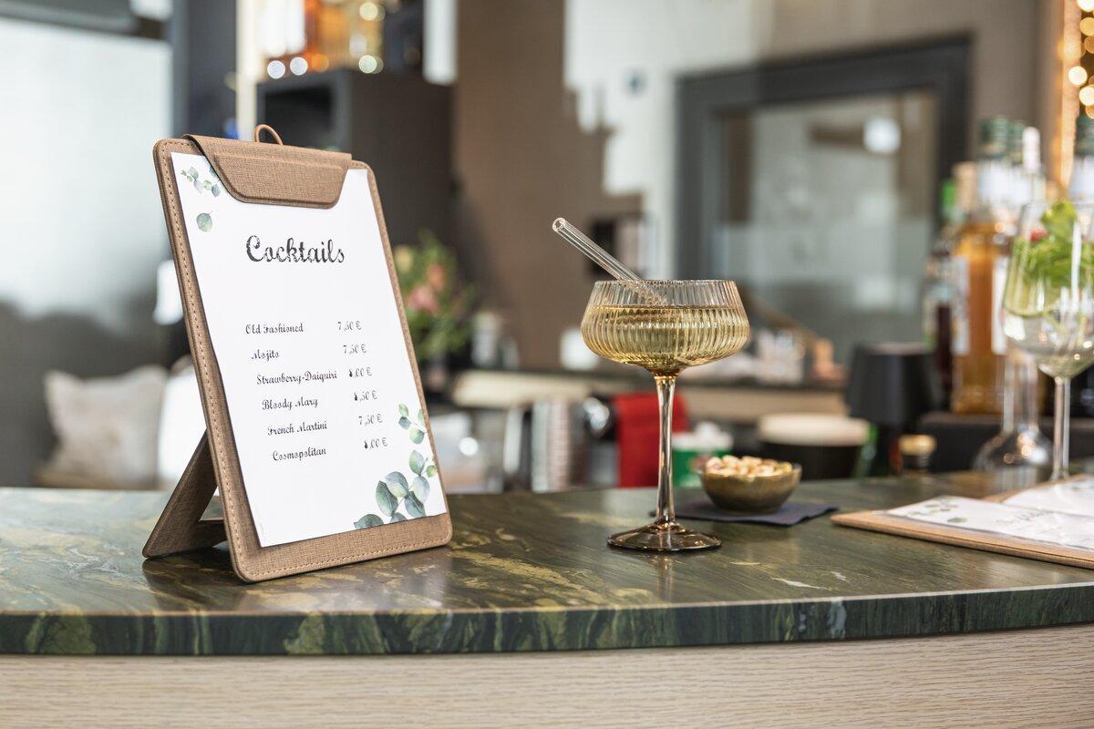 Cocktailkarte auf einer Theke, daneben ein Getränk in einem Glas mit Strohhalm