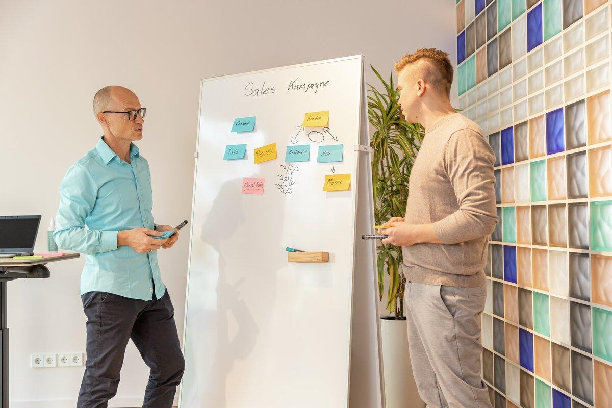 Two people discussing a sales campaign on a whiteboard with colorful sticky notes