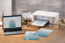 Laptop and printer printing Christmas cards on wooden desk
