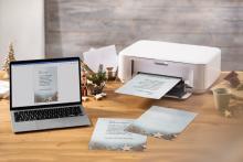 Laptop and printer on wooden table, document with Christmas motif