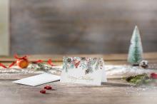 Weihnachtskarte mit Tannenzweigen und Text Merry Christmas auf Holztisch Im Hintergrund ein kleiner Weihnachtbaum