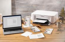 Laptop und Drucker auf Holztisch, Briefe und Stifte daneben