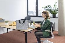 Person am Schreibtisch mit Laptop im Büro Graue Tasche im Vordergrund auf dem Tisch