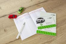 Heft mit schriftlichen Notizen, daneben zwei Spielzeugautos und ein Kugelschreiber auf Holztisch