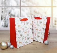 Two deer and pine needle pattern gift bags on a table in front of a snowy window