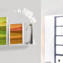 Weiße Orchidee in Metallvase, daneben bunte Bilder auf einem Regal