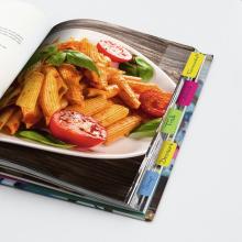 Pasta mit Tomaten und Basilikum auf Teller; geöffnetes Kochbuch mit Registerkarten