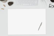 Schreibtisch mit Tastatur, Tasse, Brille, Blättern, Stift und leerem Papier