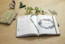 Notizbuch mit herbstlichem Motiv, Zweig und Büroklammern auf Tisch