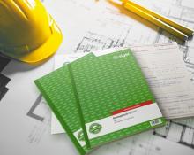 Grüner Bau-Tagebuchblock mit gelbem Helm auf Bauplänen