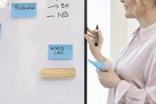 Person writing notes on whiteboard on blue sticky notes