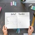 Frau hält Notizbuch mit Habit Tracker in den Händen
