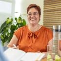 Frau in orangefarbenem Shirt und kurzen Haaren lächelt in Kamera
