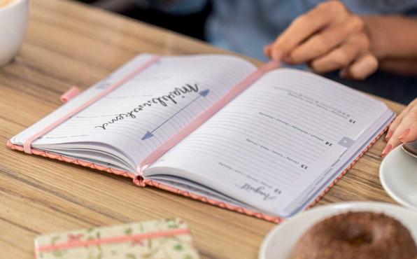 Aufgeschlagener Kalender liegt auf Tisch mit Cappuccino