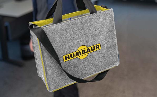 Eine hellgrau-gelbe Filztasche mit Logoaufdruck der Firma Humbauer