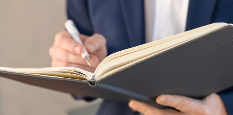 Mann notiert in aufgeschlagenes Notizbuch
