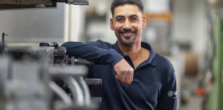 Drucker lehnt an Druckmaschine und lacht in Kamera