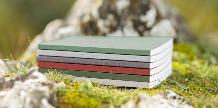 Auf einem natürlichen Untergrund mit Steinen und Moos liegt ein Stapel Notizbücher